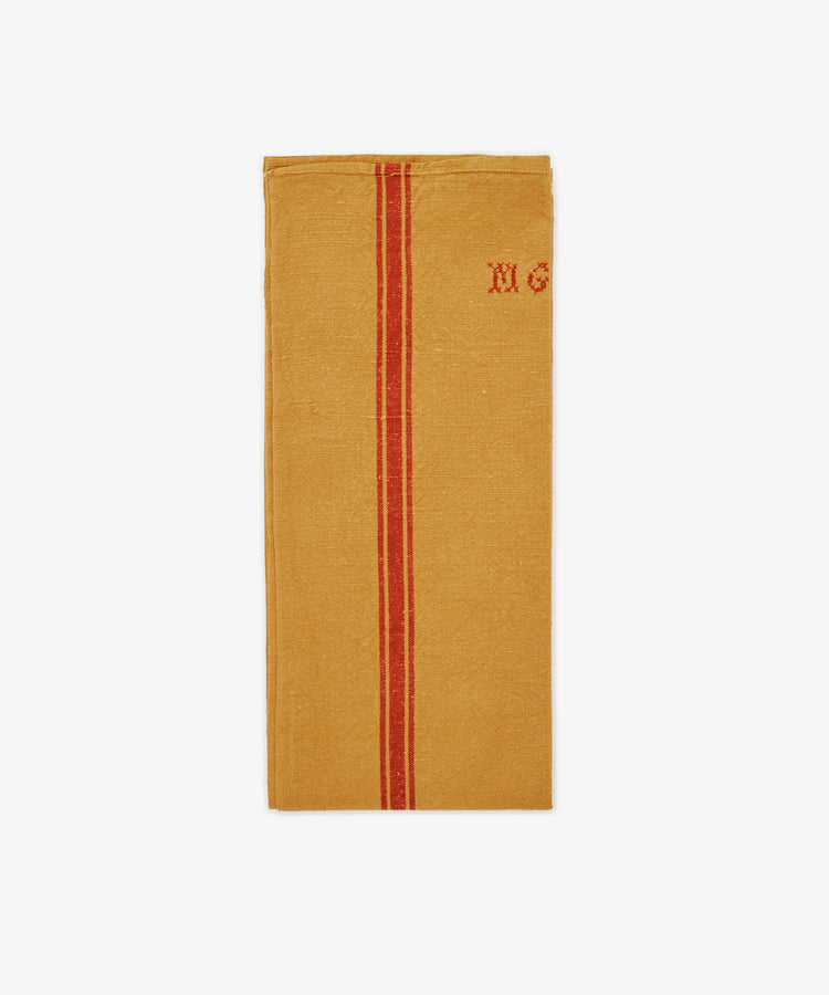 The French Vintage Tea Towel features mustard yellow linen with a central red stripe and “MG” embroidered in red in the top right, inspired by classic Provence designs—a charming accent for any kitchen.