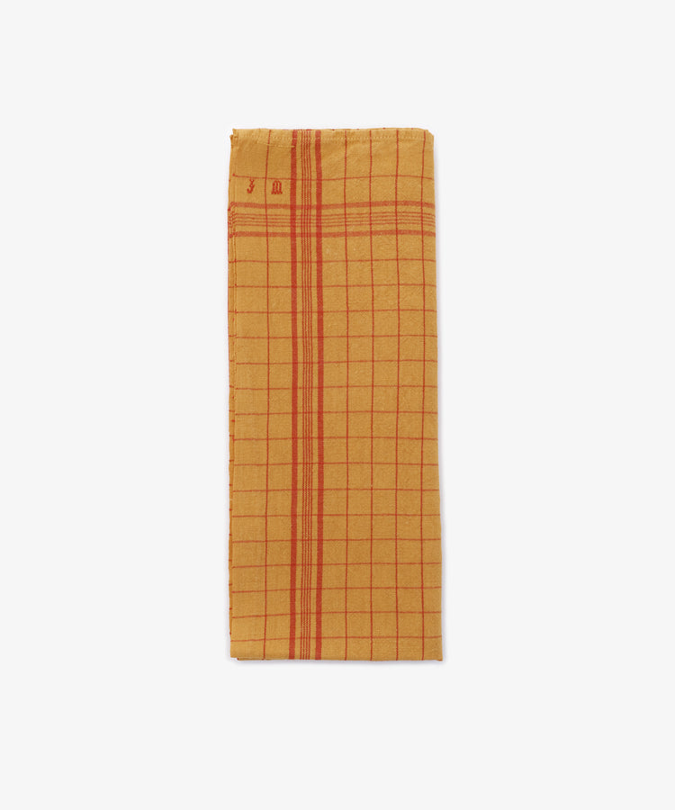 A French Vintage Tea Towel, rectangular and yellow with red grid and stripe patterns, is displayed against a white kitchen background, evoking classic Provençal style.