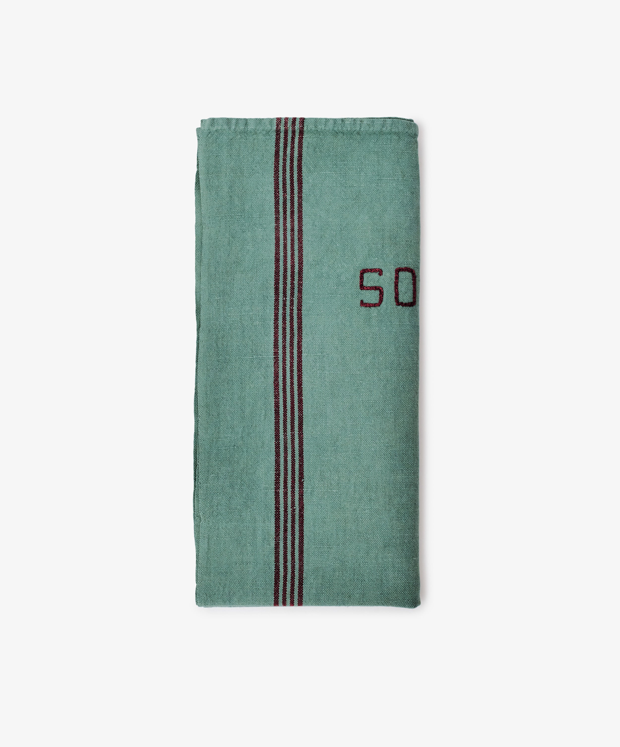 The French Vintage Tea Towel is a folded green cloth napkin with a vertical black and red stripe and partial red embroidered text on the right side, inspired by classic Provence linen, displayed on a plain white background.