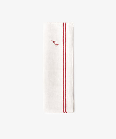 The French Vintage Tea Towel is a white linen napkin folded lengthwise with two parallel red stripes and a small red embroidered script near the top, evoking classic vintage tea towel style.