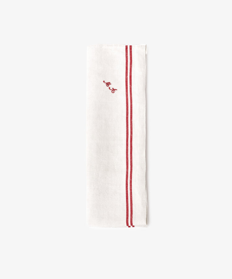 The French Vintage Tea Towel is a white linen napkin folded lengthwise with two parallel red stripes and a small red embroidered script near the top, evoking classic vintage tea towel style.
