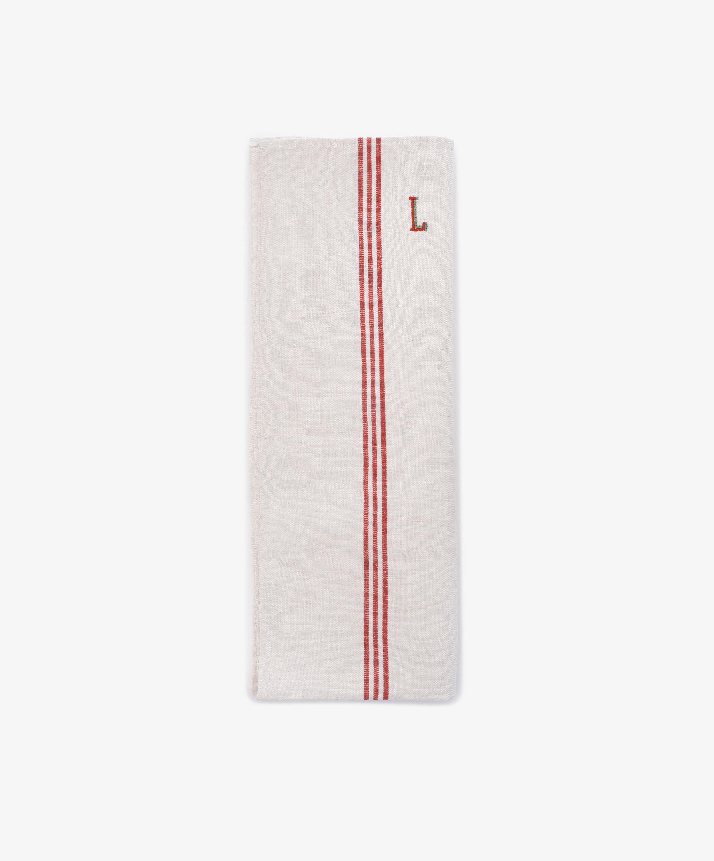 The French Vintage Tea Towel is a folded white cloth napkin with two parallel red stripes and a red embroidered letter L near the top right corner, evoking classic vintage linen tea towels.
