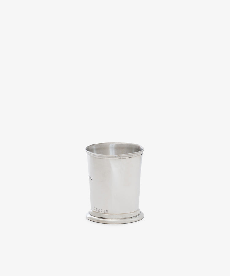 The Jane Brushes Cup, a sleek silver-toned pewter container with a slightly flared rim, sits on a white surface—ideal for holding makeup brushes in style.