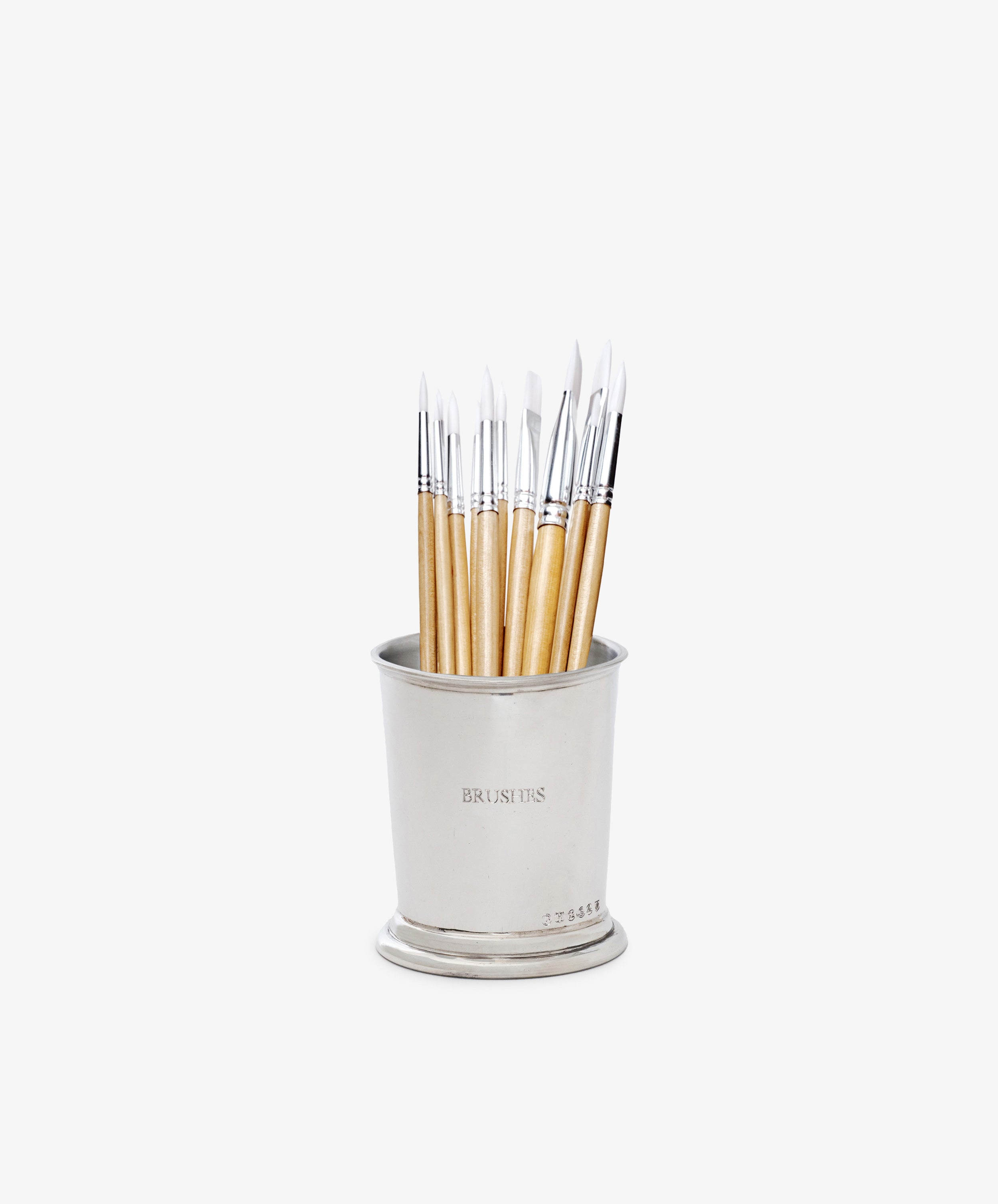 The Jane Brushes Cup is a pewter paintbrush organizer labeled BRUSH TIPS, stylishly holding light-handled brushes with white bristles, all standing upright against a white background.