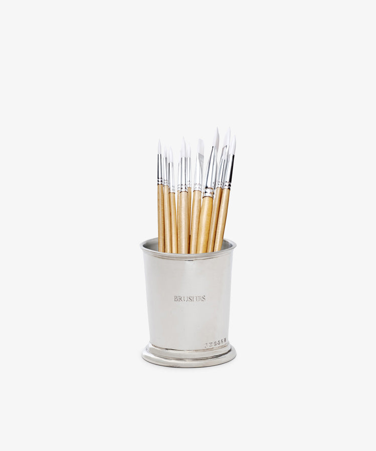 The Jane Brushes Cup is a pewter paintbrush organizer labeled BRUSH TIPS, stylishly holding light-handled brushes with white bristles, all standing upright against a white background.