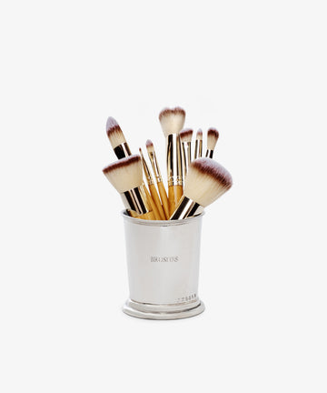 The Jane Brushes Cup holds several gold-handled makeup brushes with soft, two-toned bristles, making a chic display against a plain white background.