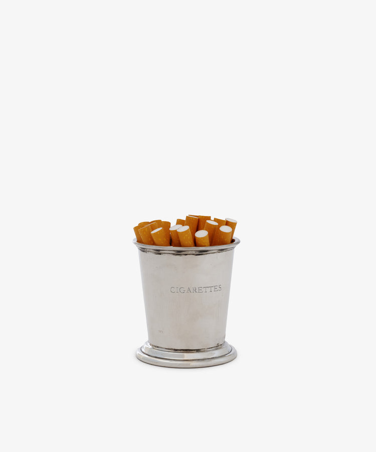 The Cleo Cigarette Cup, a silver pewter holder labeled CIGARETTES, displays several cigarette butts upright against a plain white backdrop—a distinctive piece for vintage barware collections.