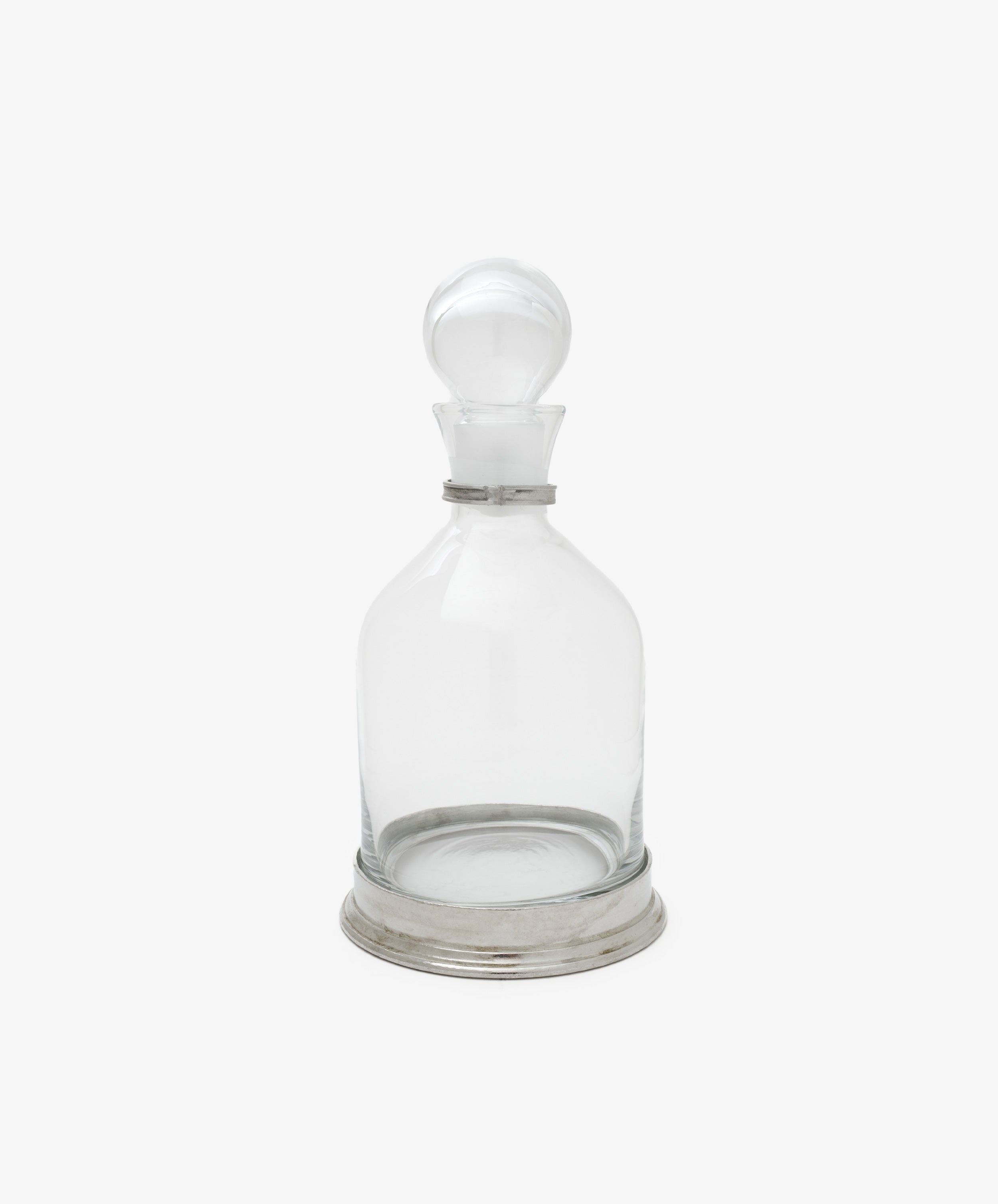 The Alec Decanter features clear glass with a pewter collar and round stopper, set on a silver-hued metal base, displayed against a plain white background.