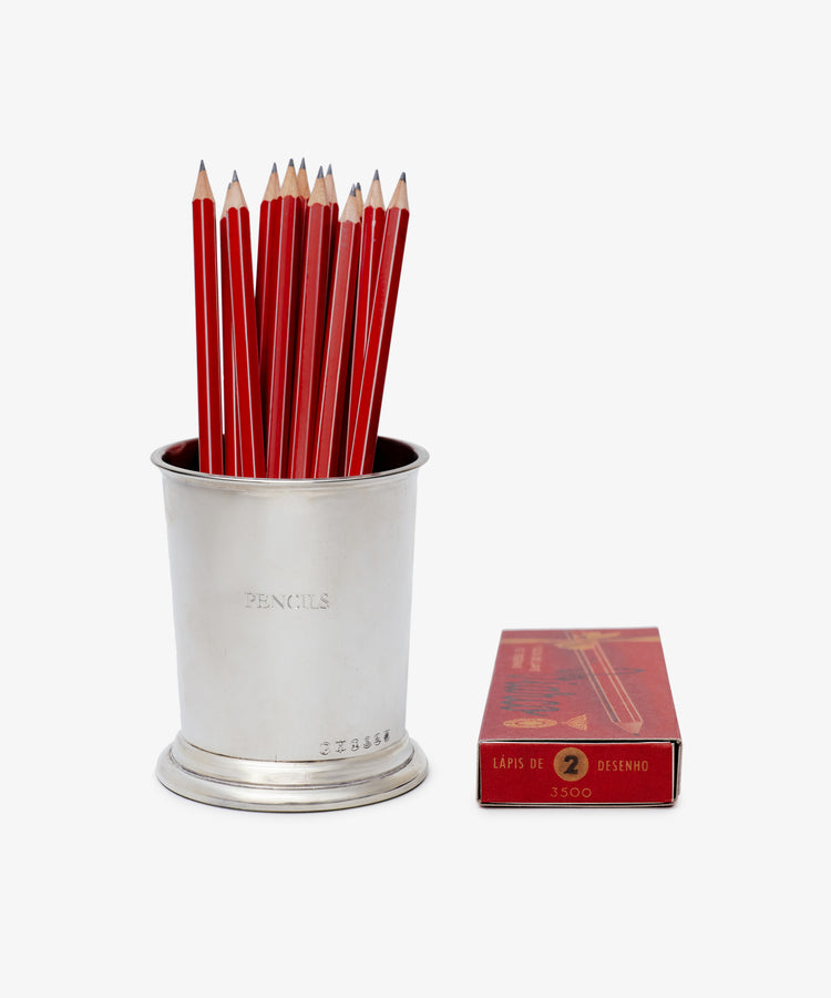 A desk essential, the Serena Pencil Cup brims with sharpened red pencils and sits beside a closed red box labeled “Lapis de Desenho 2.”.