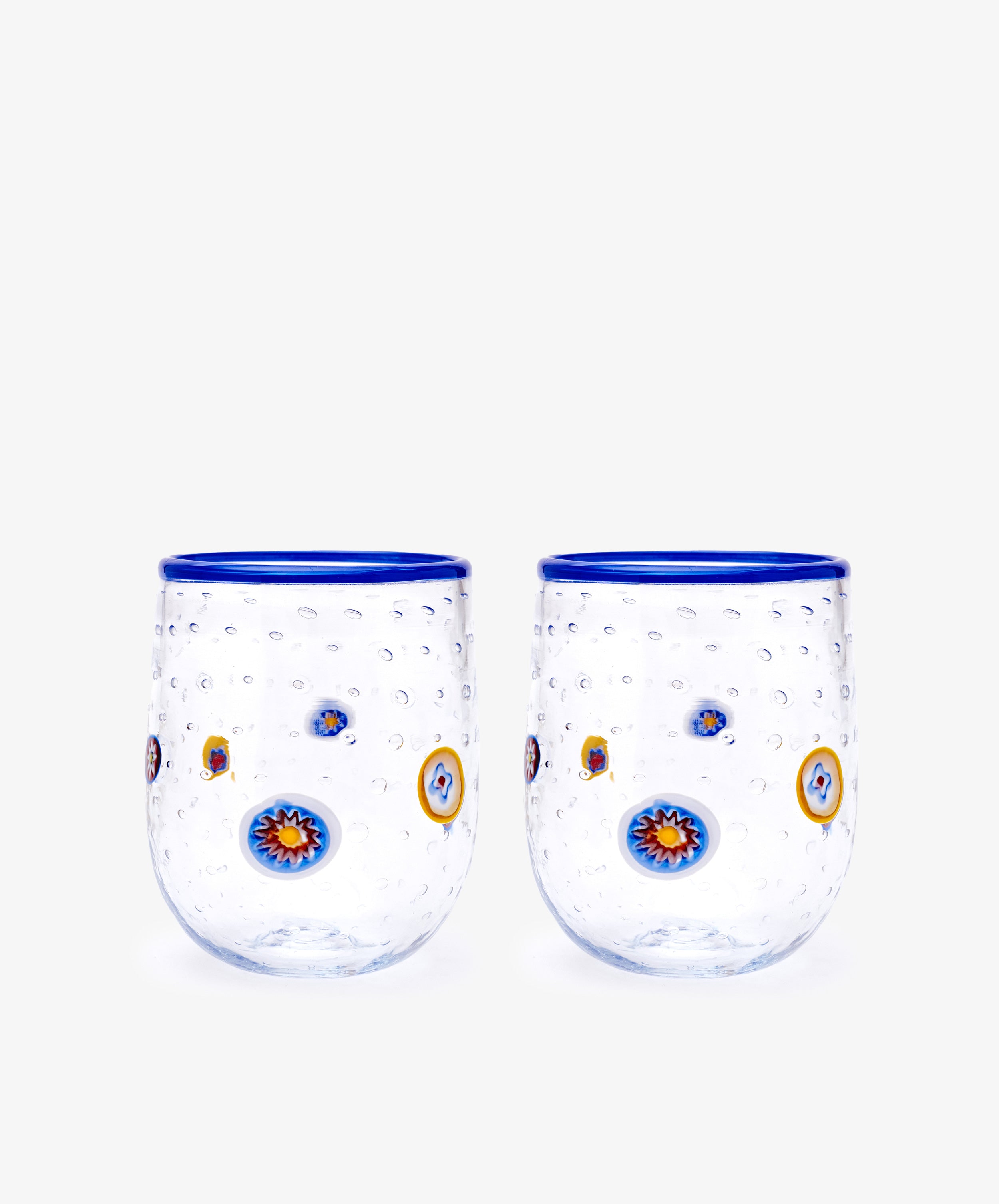 The Girotondo Glass Set of 2 features clear tumblers with blue rims, a textured surface, and vibrant circular patterns inspired by Murano glass and Venetian craftsmanship.