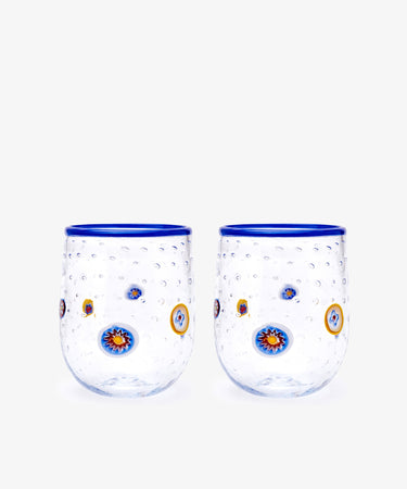 The Girotondo Glass Set of 2 features clear tumblers with blue rims, a textured surface, and vibrant circular patterns inspired by Murano glass and Venetian craftsmanship.