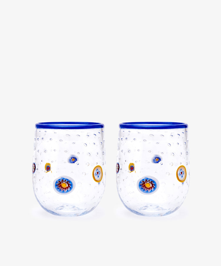 The Girotondo Glass Set of 2 features clear tumblers with blue rims, a textured surface, and vibrant circular patterns inspired by Murano glass and Venetian craftsmanship.
