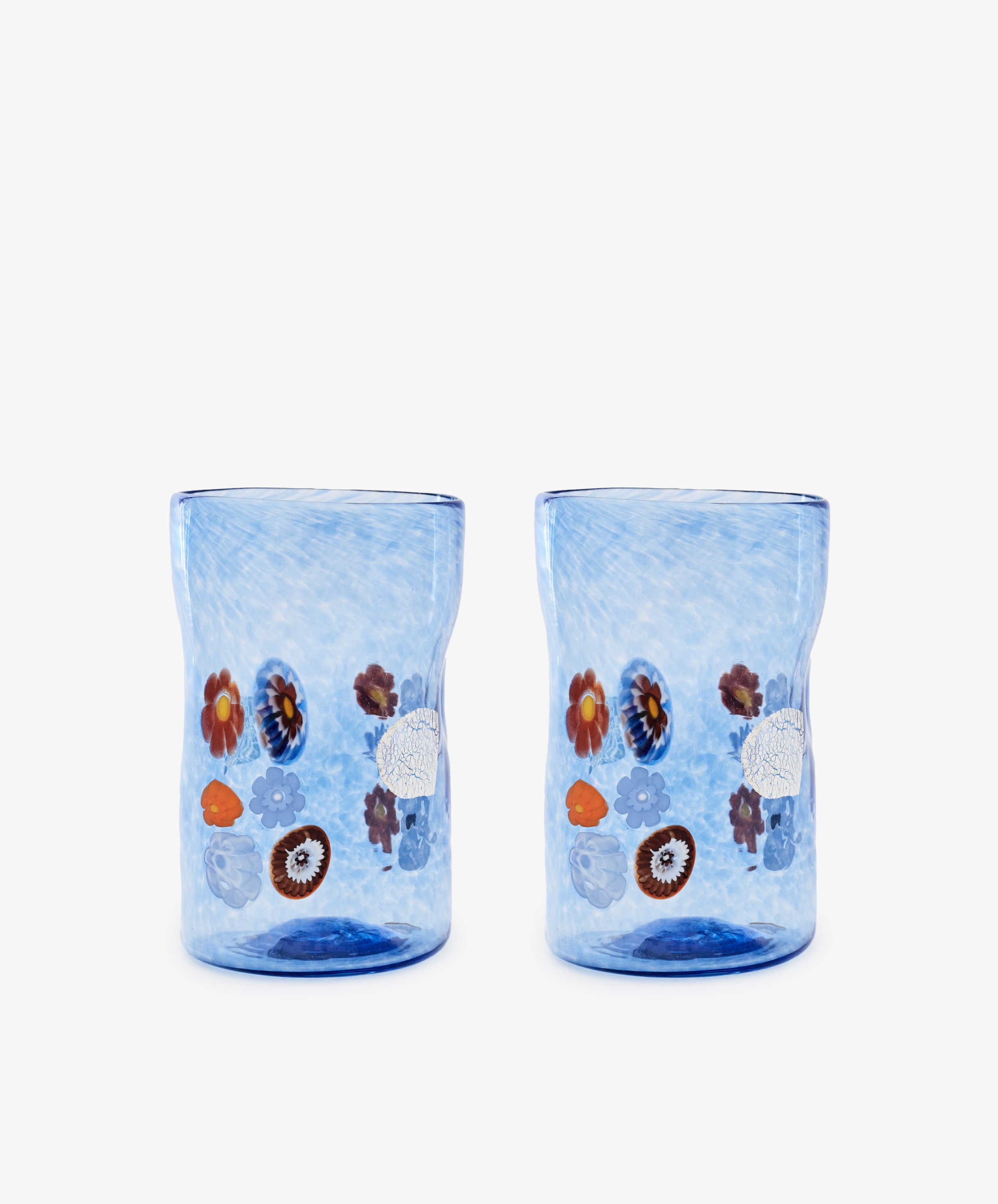The Muranesi Glass, Set of 2, features blue Murano glass tumblers with unique shapes and vibrant flower and fruit motifs, shown on a plain white background.