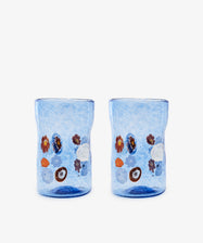 The Muranesi Glass, Set of 2, features blue Murano glass tumblers with unique shapes and vibrant flower and fruit motifs, shown on a plain white background.