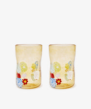 The Muranesi Glass Set of 2 features yellow handblown tumblers with a unique shape, each adorned with vibrant red, blue, green, and white floral patterns near the base—classic Murano-inspired elegance.