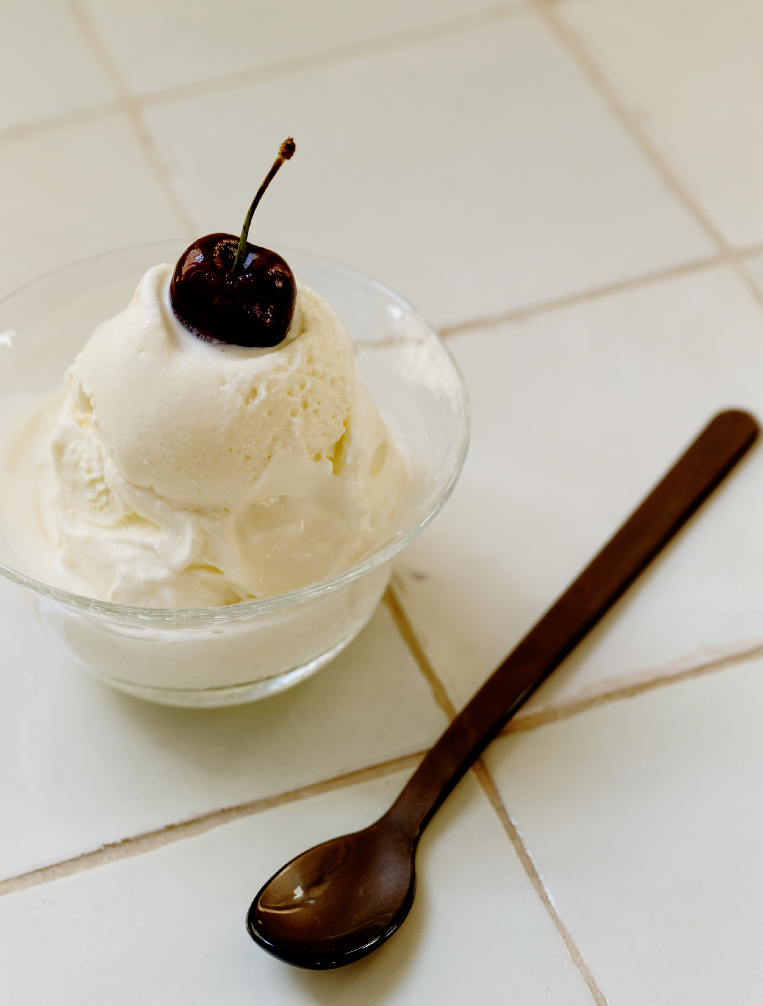 A Sweet Treat Bundle holds a scoop of vanilla ice cream with a cherry on top, beside a dark Lungo spoon on a tiled surface.