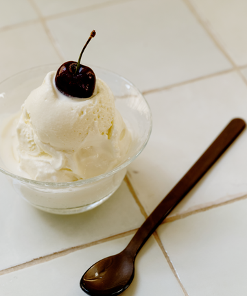 A Sweet Treat Bundle holds a scoop of vanilla ice cream with a cherry on top, beside a dark Lungo spoon on a tiled surface.