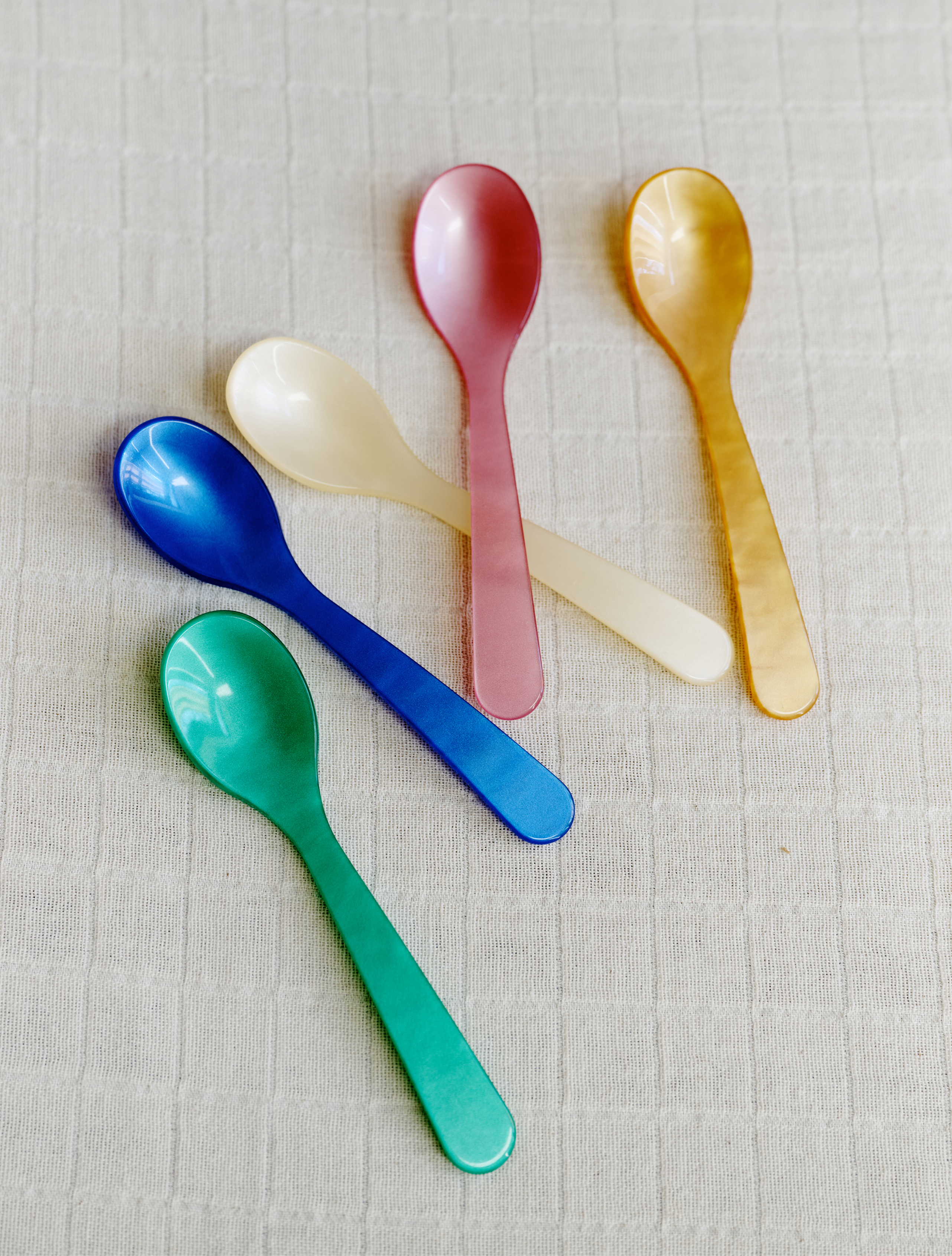 Five colorful spoons from the Spooning Bundle in green, blue, white, pink, and yellow rest on a light textured fabric—perfect for adding charm to any Valentine’s Day set.