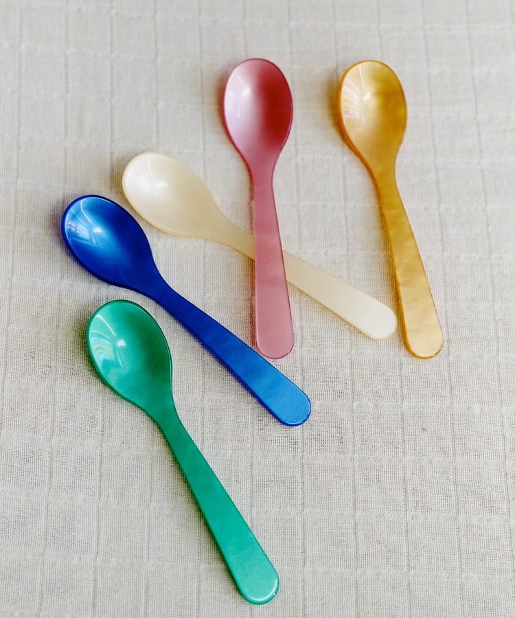 Five colorful spoons from the Spooning Bundle in green, blue, white, pink, and yellow rest on a light textured fabric—perfect for adding charm to any Valentine’s Day set.