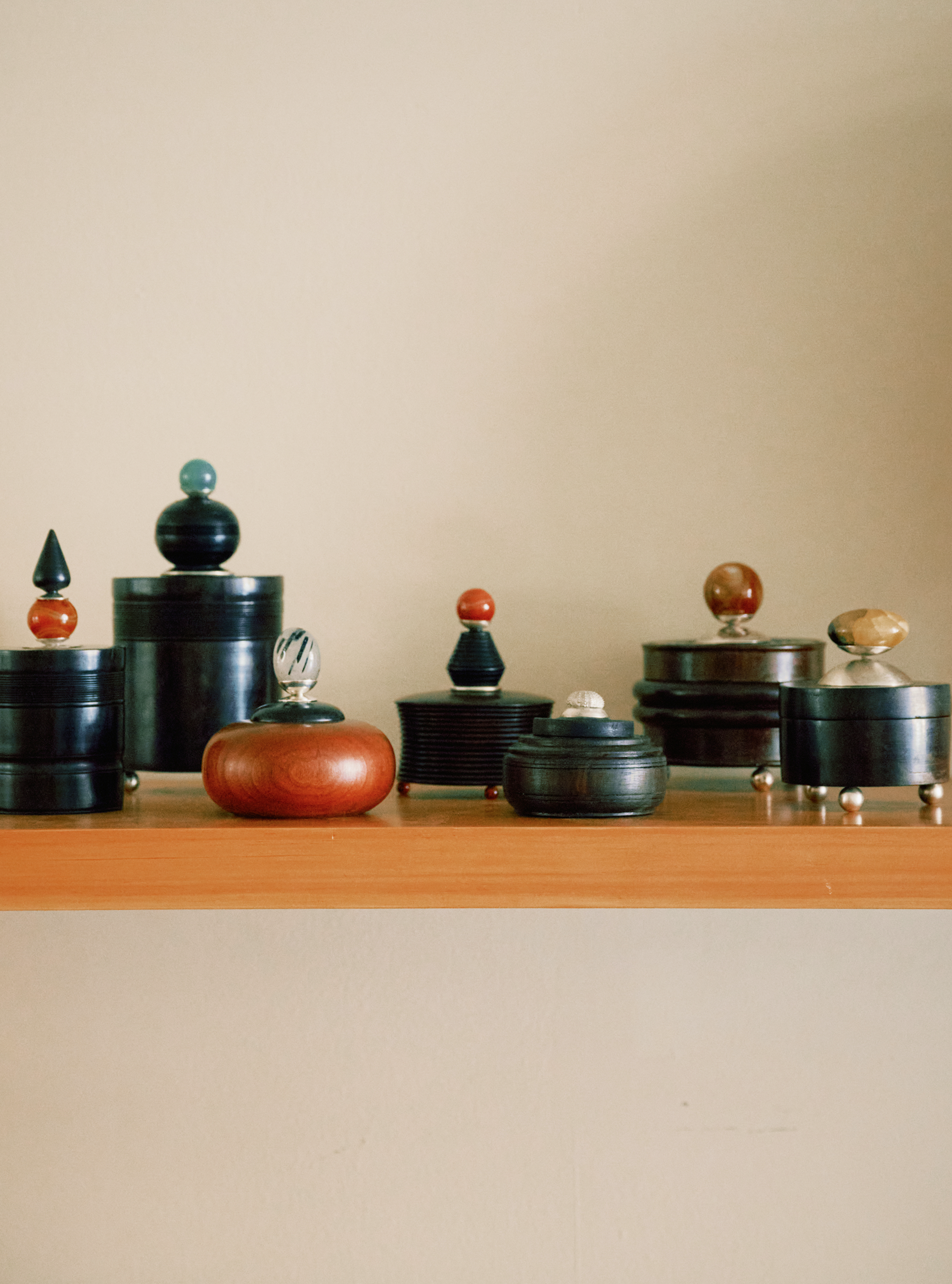 The Curiosity Box, a decorative wooden container with a unique knob lid, sits arranged on a light wooden shelf against a plain beige wall.