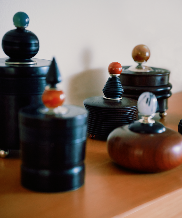 A Curiosity Box, a round wooden container with a decorative lid and colorful knob, is arranged on a wooden surface against a plain background.