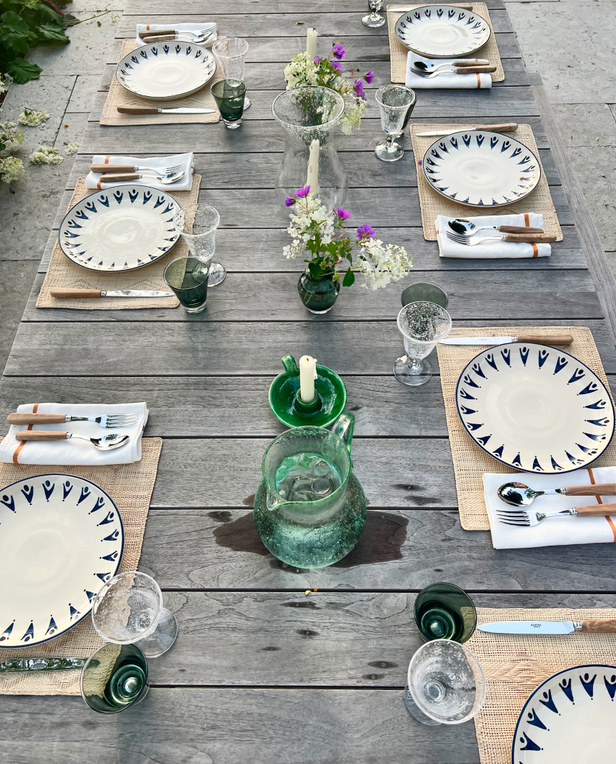 Elegant outdoor table setting with patterned plates, green glassware, and fresh flowers, bowls of soup