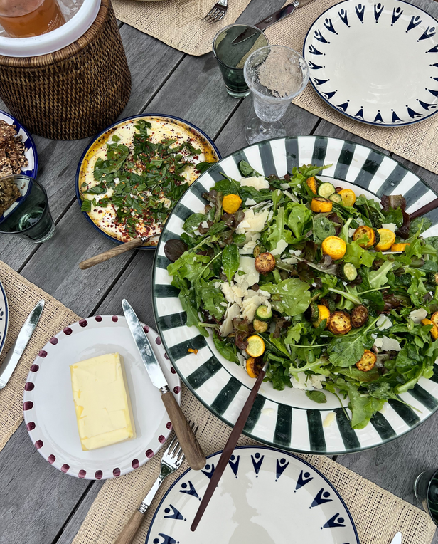 Elegant outdoor table setting with patterned plates, green glassware, and a bowl of salad