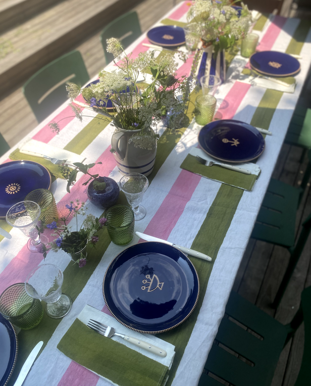 Colorful outdoor table with navy plates, striped pink and green tablecloth, and fresh greenery.