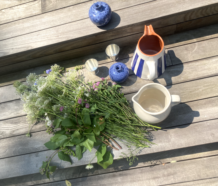 Wildflowers with ceramic pitchers, blue vases, and metal cups on wooden steps.
