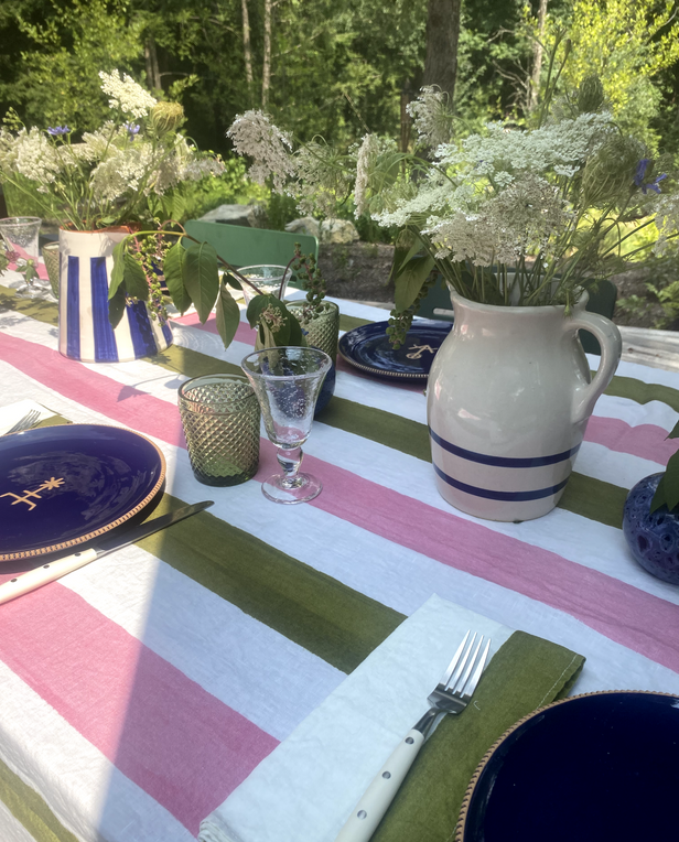 Colorful outdoor table with navy plates, striped pink and green tablecloth, and fresh greenery.