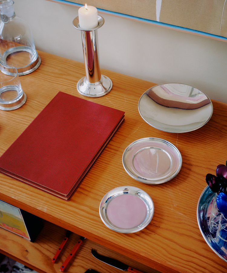 A red book, three Elena Bowls, a candle in a holder, and glassware are arranged on a wooden surface.