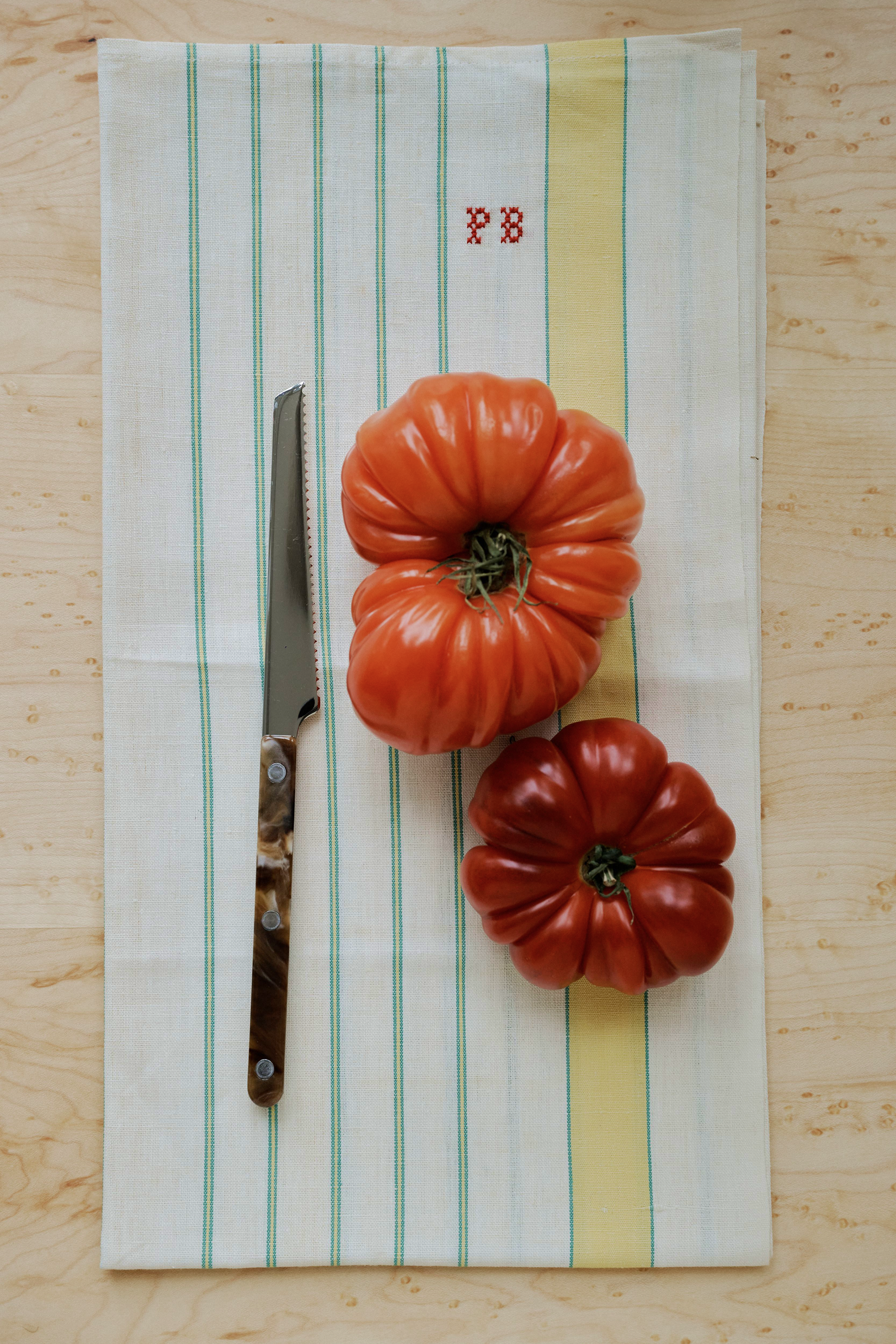 Two large heirloom tomatoes and a Tomato Knife sit on a striped kitchen towel with red 