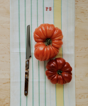 Two large heirloom tomatoes and a Tomato Knife sit on a striped kitchen towel with red 