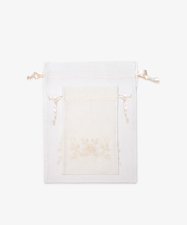 Two Linen Drawstring Bags, handmade in Portugal, feature cream floral designs and satin ribbon ties. The smaller bag rests atop the larger against a plain backdrop.