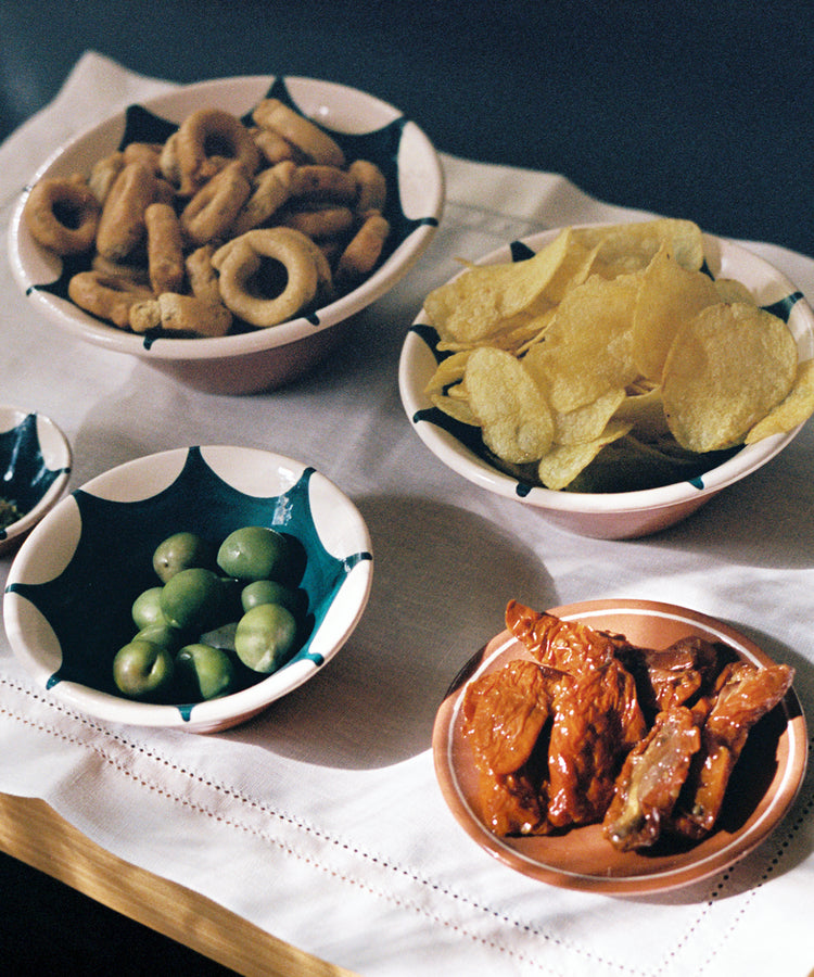 Lorna Hemstitch Placemat sits on table and holds various ceramic bowls of snacks.