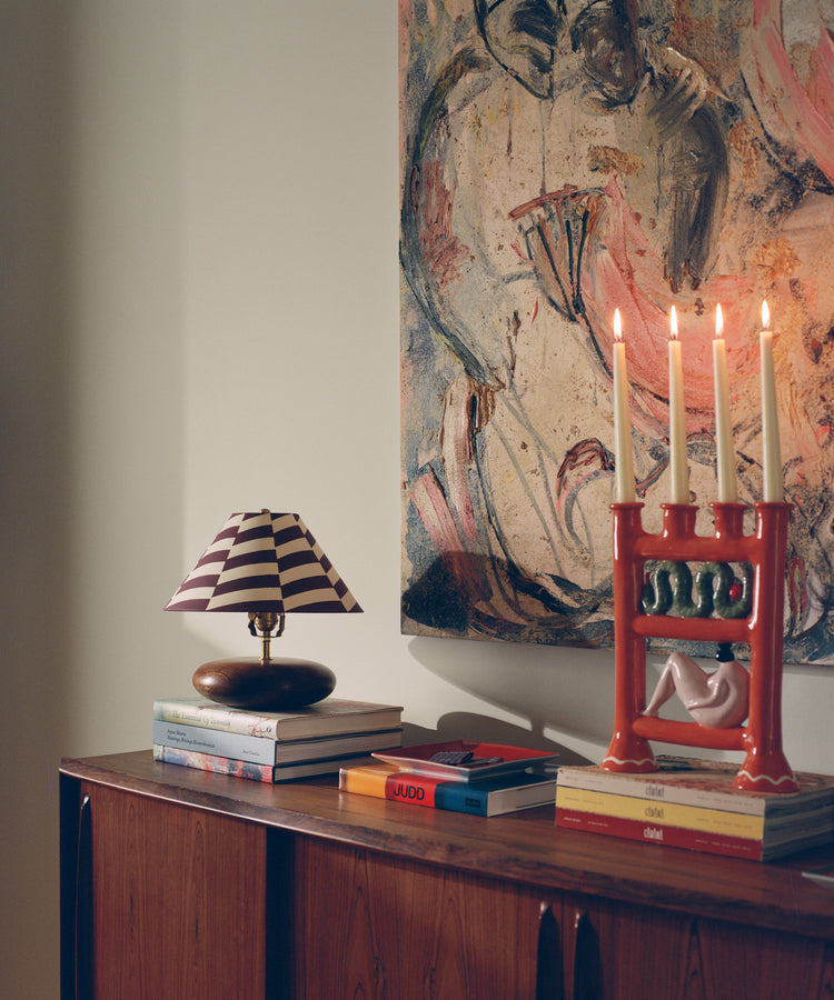 Eve Candle Holder in situ with lit candles on a wooden sideboard, joined by lamp and stacks of books.