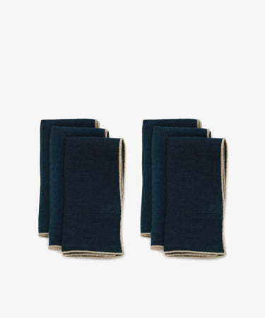 Venise Napkin. Two rows of three folded rectangular napkins in deep blue linen with cream stitched hems.