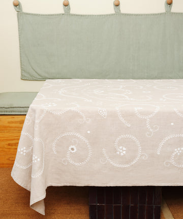 Tan and white Inez Tablecloth in situ, spread over table with green wall hanging and bench.