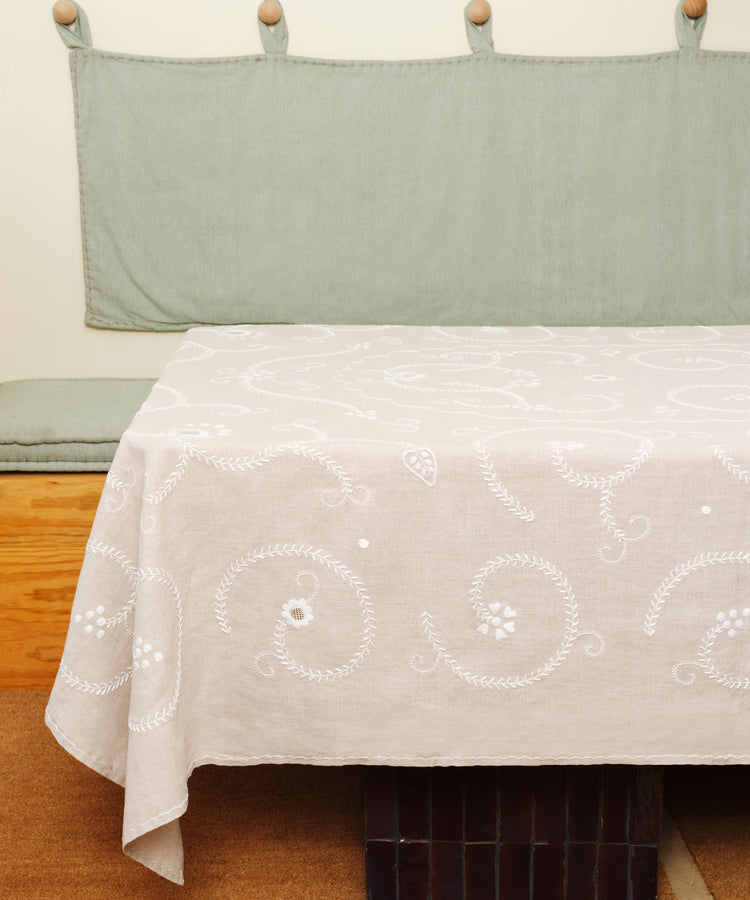 Tan and white Inez Tablecloth in situ, spread over table with green wall hanging and bench.