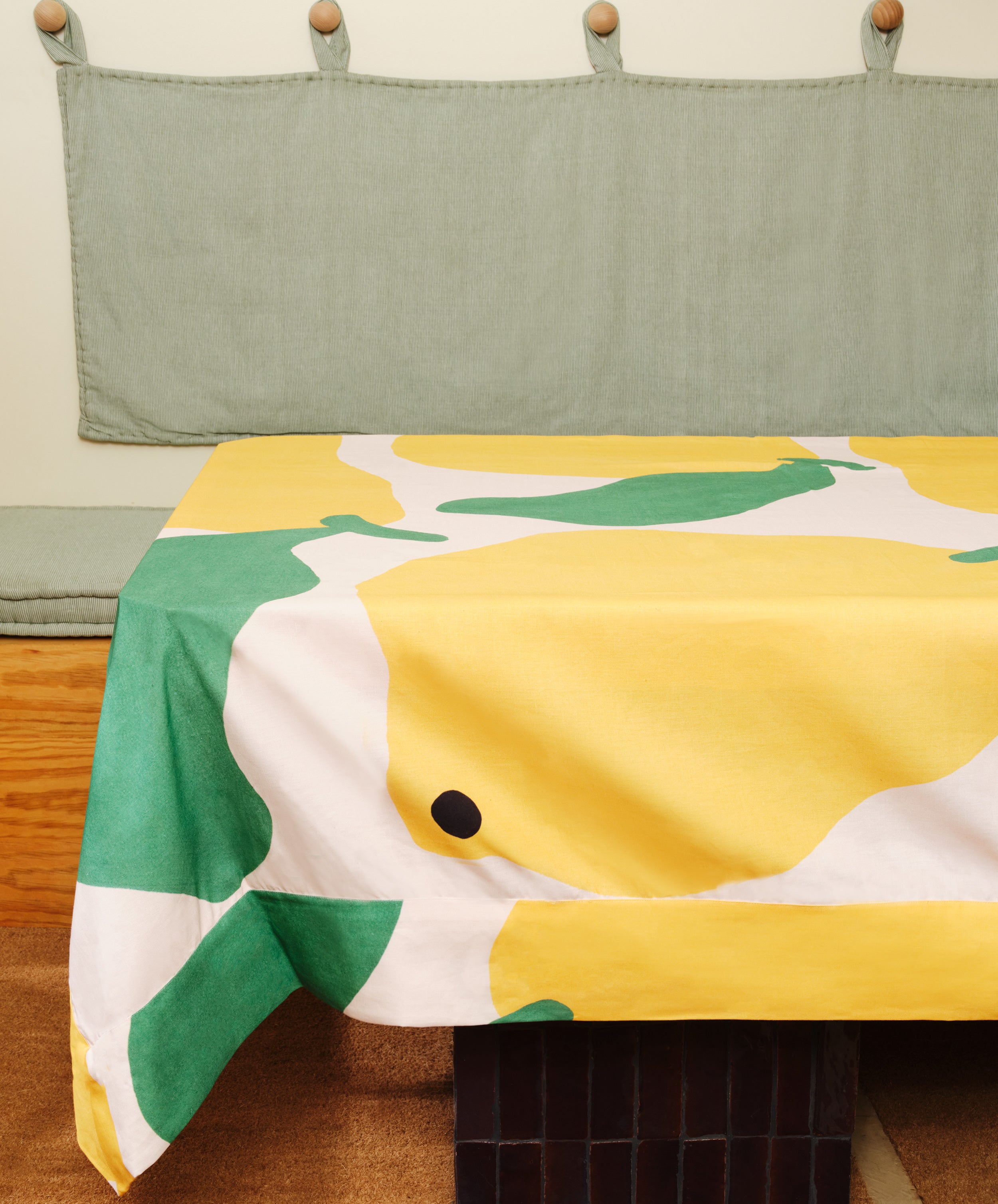 Main Squeeze Tablecloth draped over table, printed with oversized yellow and green citrus motif.