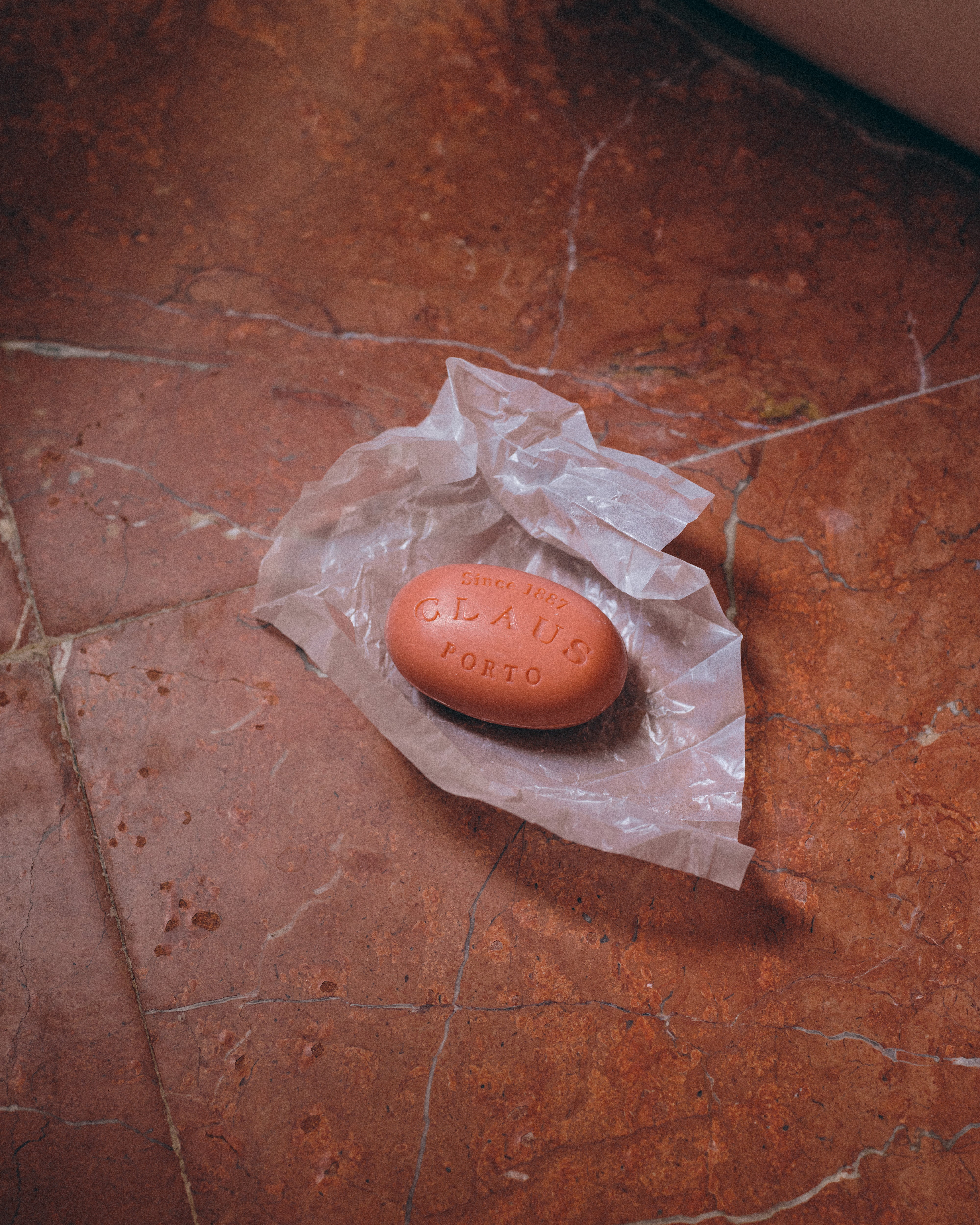 Pink oval bar of soap sits on open wrapper on striated terra cotta tile floor.