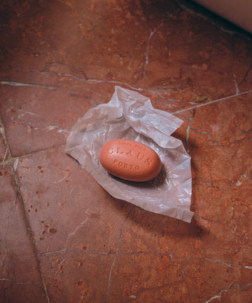 Pink oval bar of soap sits on open wrapper on striated terra cotta tile floor.