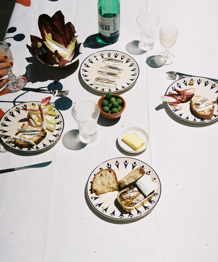 Tablescape on white cloth with Vito Dinner Plates, bread, tinned fish, and olives.