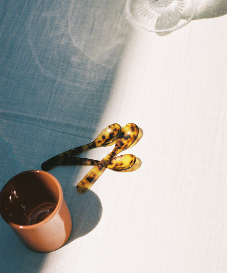Group of Piccolo Spoons on white tablecloth near terracotta mug.