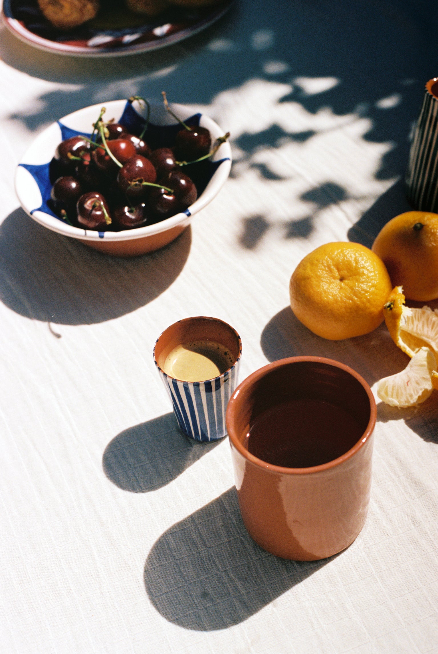 Blue espresso cup on outdoor tablescape with cherries and clementines.