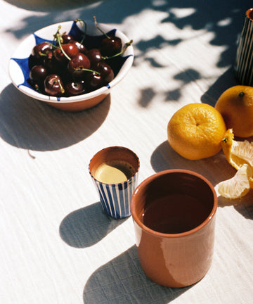 Blue espresso cup on outdoor tablescape with cherries and clementines.