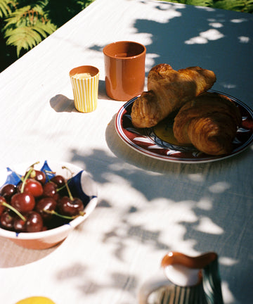Yellow espresso cup on outdoor tablescape with croissants and cherries.