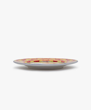 Palio Dinner Plate. Glazed ceramic in red and yellow designs with snail motif, angled side view.