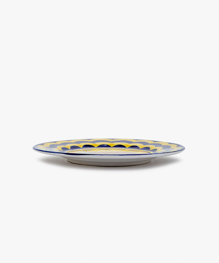Palio Dinner Plate. Glazed ceramic  in yellow and navy designs with tortoise motif, angled side view.