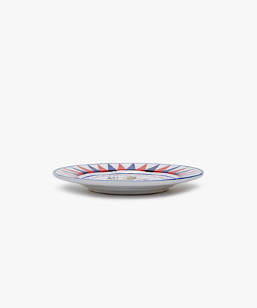 Palio Small Plate in white glazed ceramic with blue and red designs, side view.